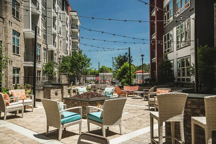 Chic apartment courtyard with stylish seating, vibrant greenery, and festive string lights, perfect for social gatherings.
