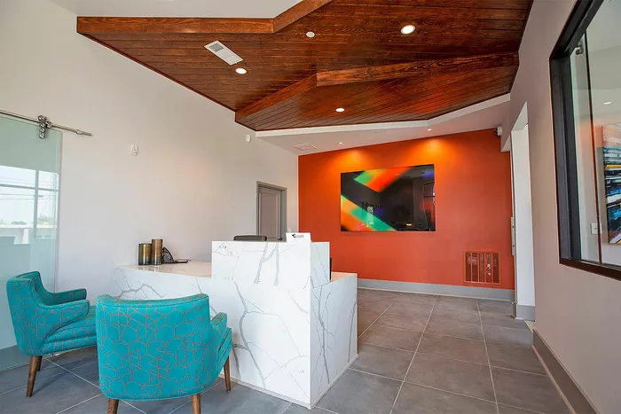 Modern lobby area featuring vibrant teal chairs, a sleek marble reception desk, and a bold orange accent wall with colorful artwork.