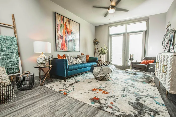 Modern living room with vibrant artwork, elegant blue sofa, and geometric coffee table on a stylish patterned rug.