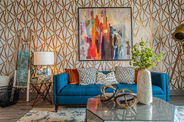 Vibrant living room with a modern blue sofa, abstract wall art, and patterned wallpaper. Stylish decor includes a chic lamp, decorative pillows, and a lush green plant.
