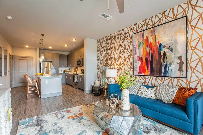 Modern open-plan living space featuring a cozy blue sofa, eclectic wall art, and stylish kitchen with sleek cabinetry and pendant lighting.