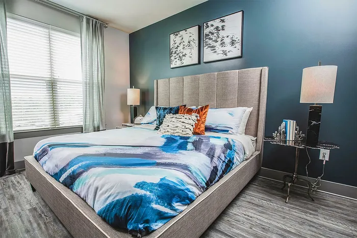 Elegant bedroom featuring a modern bed with vibrant blue bedding, stylish decor, and ample natural light from large windows.