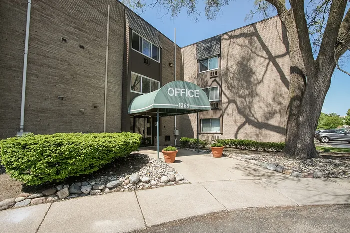 Inviting apartment building entrance with a green awning labeled 'Office,' surrounded by lush greenery and neatly maintained landscaping.