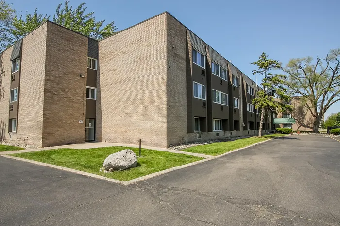 Charming three-story brick apartment building with modern windows and lush greenery, offering ample parking space and inviting atmosphere.
