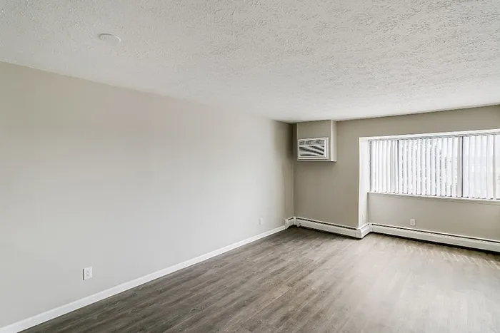 Bright and spacious living room with large window, sleek hardwood floors, and modern neutral walls, perfect for contemporary living.