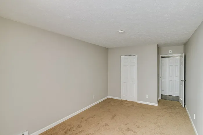 Bright and cozy room with fresh neutral walls, plush carpet, and modern closet doors, perfect for personalization.