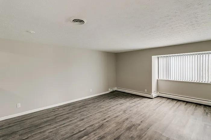 Spacious living room with sleek wooden flooring and large window offering ample natural light and modern appeal.