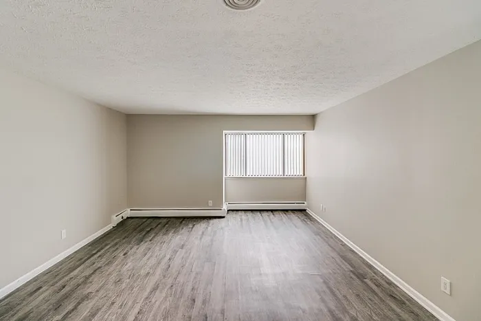 Spacious and bright living room with elegant wood flooring, neutral walls, and abundant natural light from a large window, perfect for a comfortable and modern living experience.