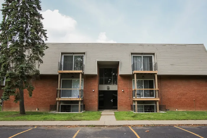 Charming brick apartment building with private balconies and lush green surroundings.