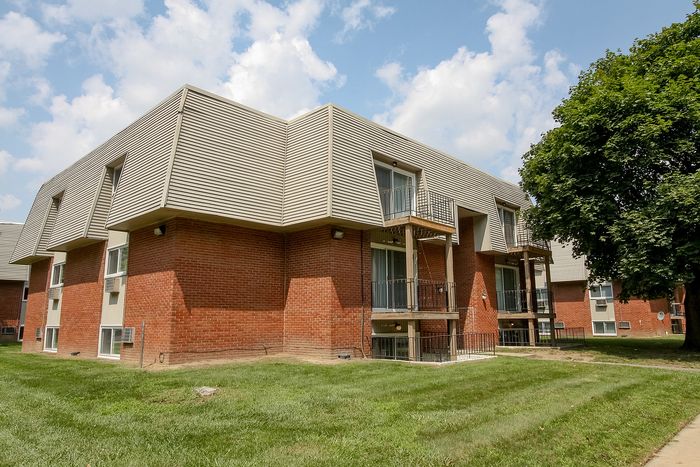 Charming apartment complex exterior with modern brick design, lush green surroundings, and private balconies.