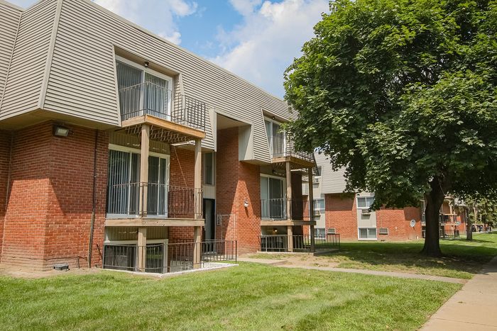 Inviting apartment complex with charming brick exterior, private balconies, and lush green surroundings.