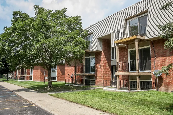 Charming brick apartment complex with private balconies and lush green surroundings, perfect for comfortable living.