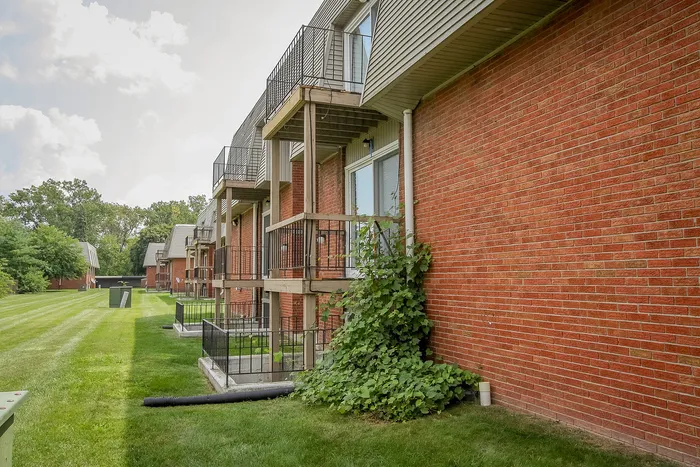Charming apartment complex with private balconies, nestled in a lush green setting with well-maintained lawns and brick facades.