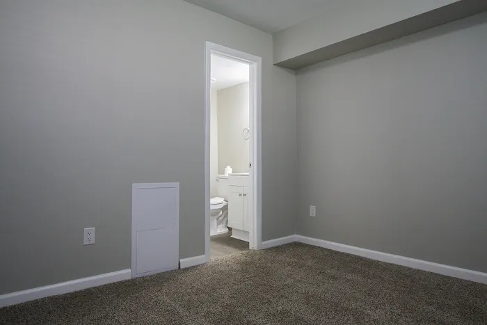 Cozy room with soft carpet, leading to a modern bathroom featuring sleek cabinetry and fixtures.