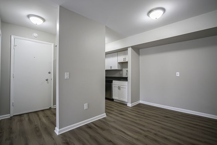 Modern apartment entrance with sleek laminate flooring and a bright, open-concept kitchen featuring white cabinetry and stainless steel accents.