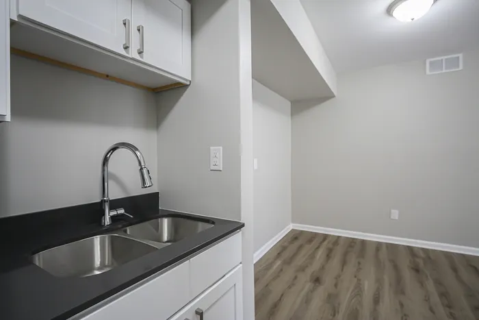 Sleek modern kitchen area featuring stainless steel double sink, elegant faucet, and crisp white cabinetry against a stylish neutral backdrop.
