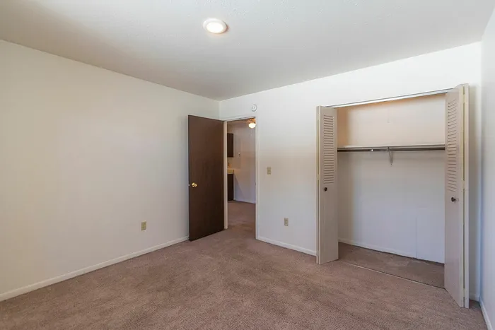 Spacious bedroom with plush carpet, an open closet, and ample natural light, perfect for comfortable living.