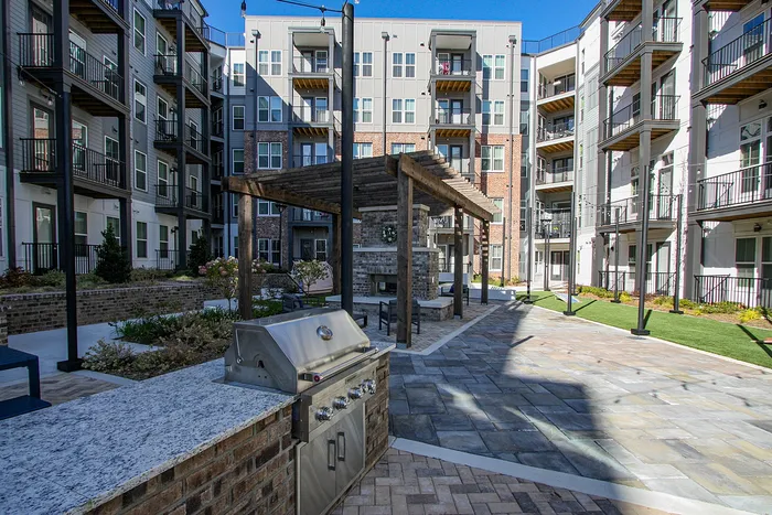 Modern apartment complex featuring outdoor grilling area and elegant courtyard with seating, surrounded by stylish multi-story buildings.