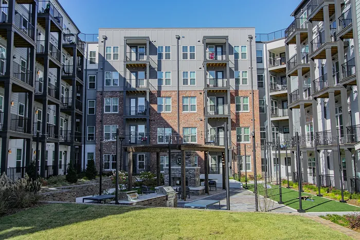 Modern apartment building exterior with spacious balconies overlooking a well-maintained courtyard featuring a cozy seating area and lush greenery.