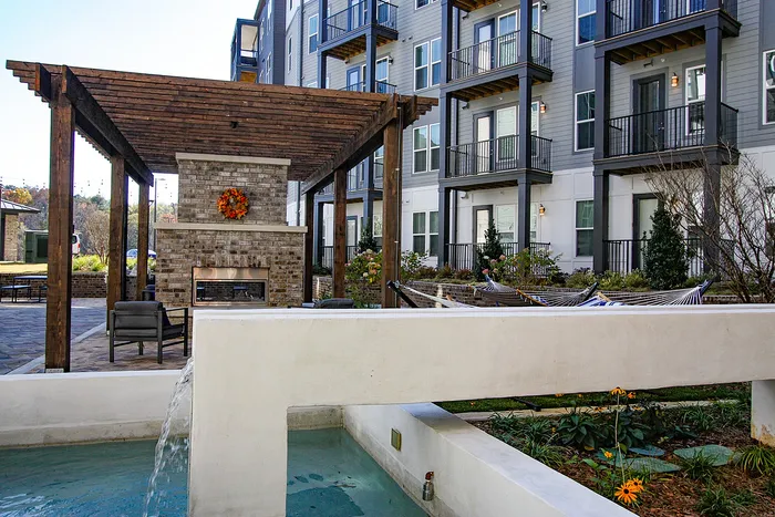 Chic apartment complex with a cozy outdoor fireplace, modern hammocks, and a peaceful water feature.