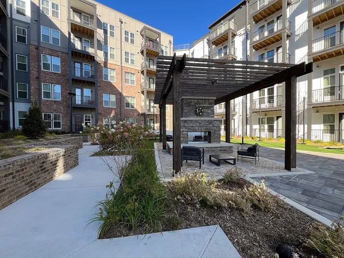 Chic apartment complex featuring modern architecture with private balconies, lush landscaped gardens, and a stylish outdoor seating area under a wooden pergola.