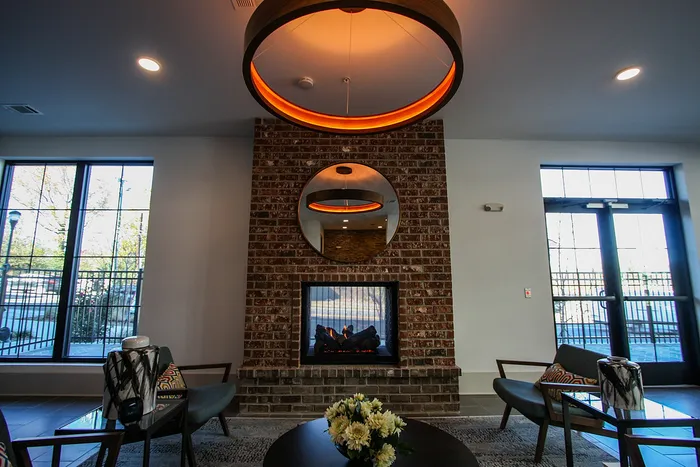 Cozy apartment lounge with brick fireplace, modern seating, and large windows for natural light.