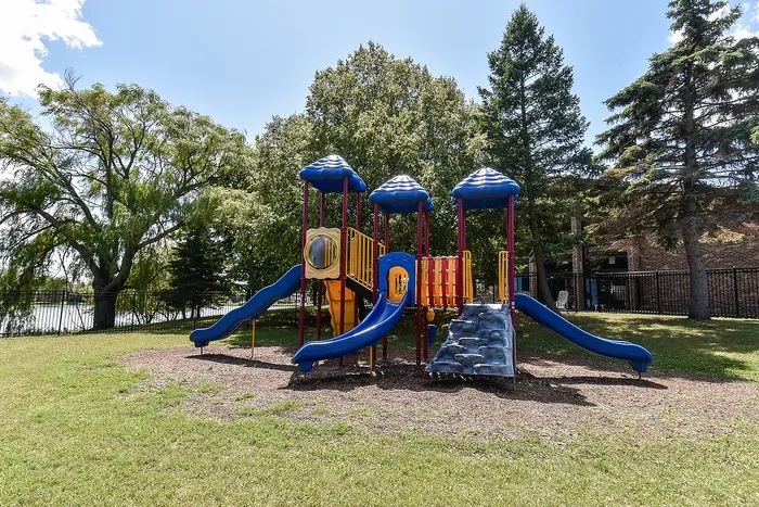 Vibrant playground with blue slides and climbing areas, nestled among lush green trees, offering a perfect space for children to play and explore.