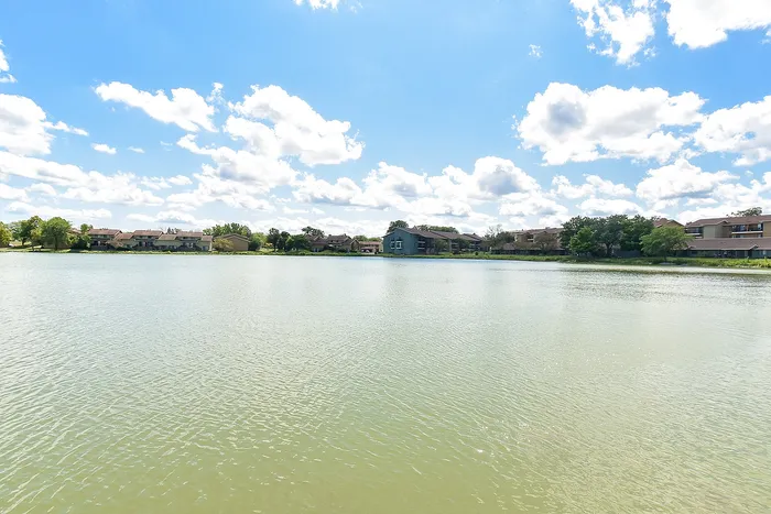 Breathtaking lakeside view with charming homes under a vibrant blue sky and fluffy white clouds.