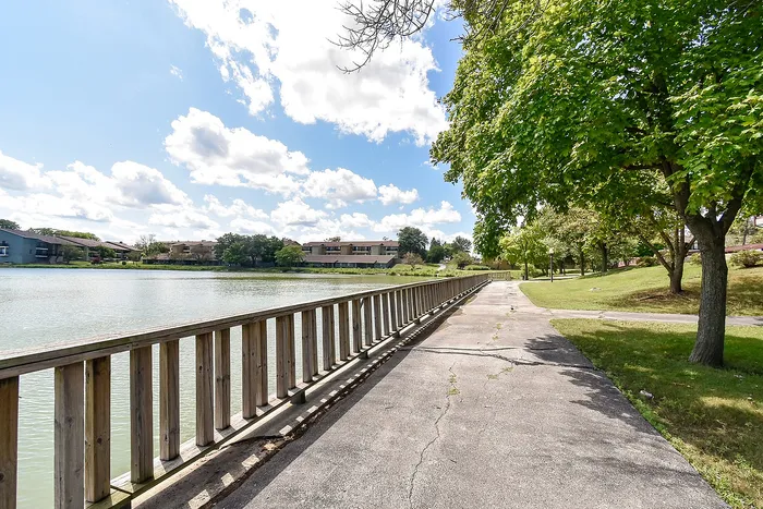 Charming lakeside scenery with a picturesque pathway and vibrant green trees, ideal for tranquil strolls and outdoor relaxation.