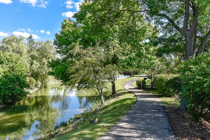 Charming riverside pathway flanked by lush greenery under a bright blue sky, perfect for serene strolls.