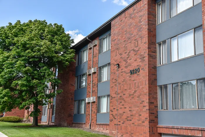 Charming brick apartment building with large windows, inviting green surroundings, and a peaceful residential feel.