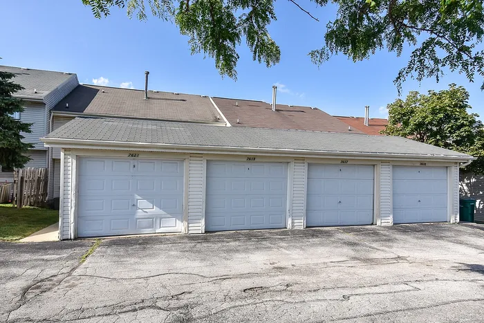 Charming townhouse garages with four pristine white doors, surrounded by lush greenery under a clear blue sky.