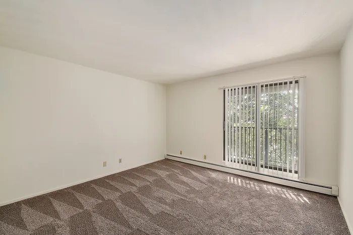 Bright, spacious living area with plush carpet and floor-to-ceiling windows offering serene outdoor views.