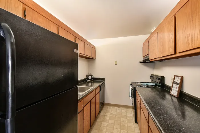 Cozy and efficient kitchen with sleek black appliances, charming wooden cabinetry, and ample counter space against a warm, inviting backdrop.
