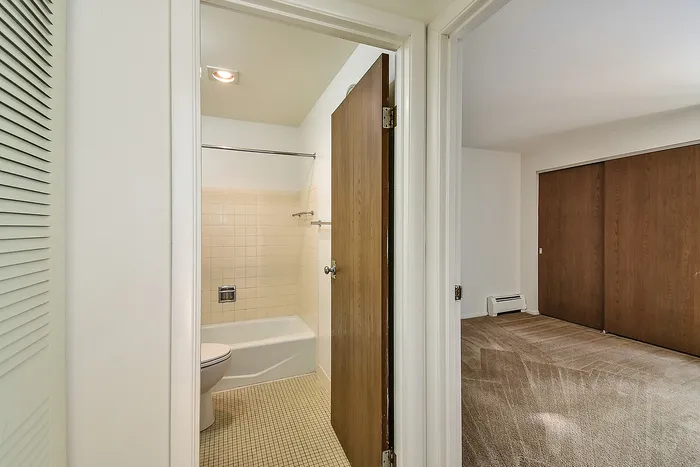 Inviting apartment interior showcasing a pristine bathroom with beige tiles and a cozy, carpeted bedroom with ample closet space.