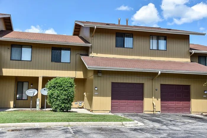 Charming townhouse exterior with a warm, inviting facade and twin garage doors, nestled under a clear blue sky.