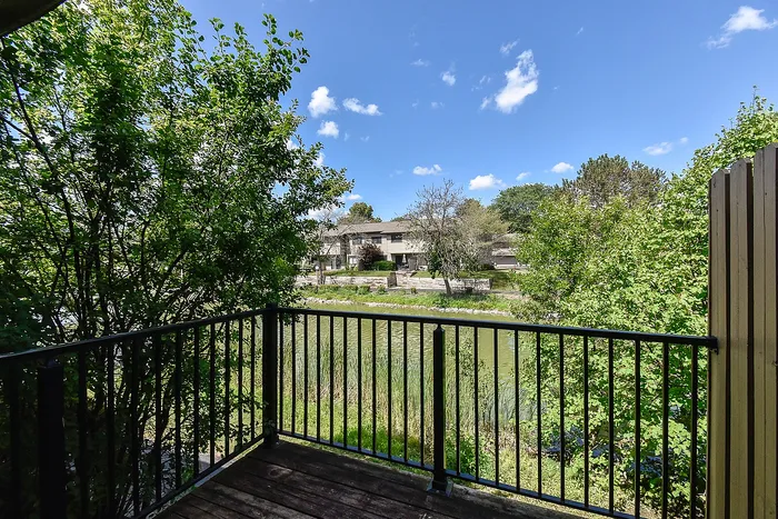 Charming balcony view overlooking lush greenery and a tranquil pond under a vibrant blue sky.