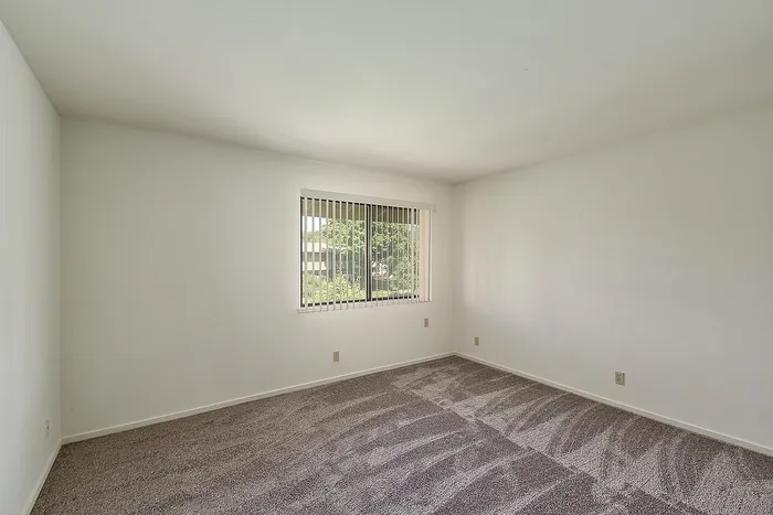 Bright, spacious bedroom with fresh carpet and a large window offering serene garden views.