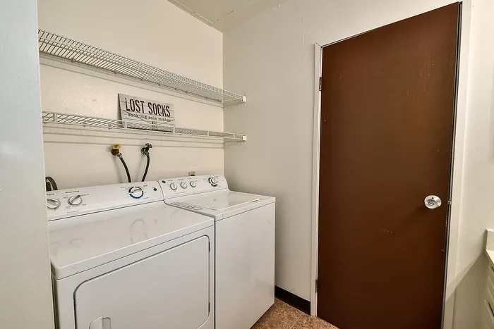 Bright laundry room with convenient washer and dryer, featuring ample shelving for storage.