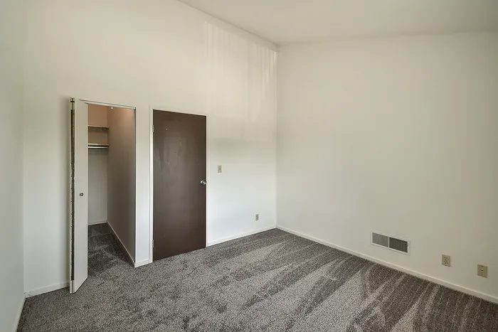 Inviting bedroom with plush carpet, large closet, and sleek brown door, perfect for comfortable living.