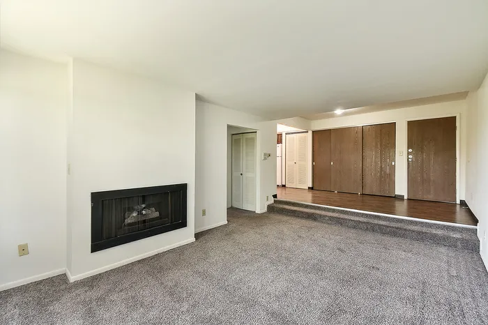 Inviting open living space with a cozy fireplace, plush carpet, and elegant wood flooring, perfect for modern living.