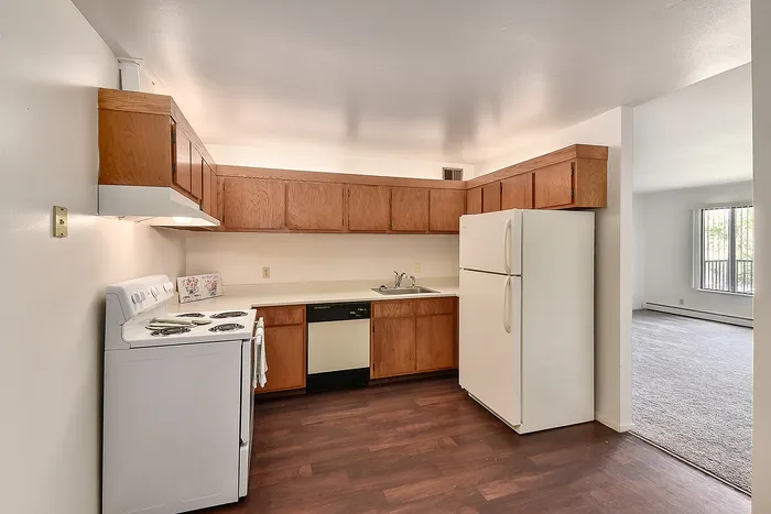 Inviting kitchen with warm wooden cabinets, sleek white appliances, and an open floor plan leading to a sunlit living area.