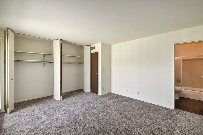 Spacious bedroom with plush carpeting, abundant closet space, and an ensuite bathroom in a modern apartment.