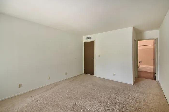 Bright, spacious room with fresh carpet and an inviting open doorway leading to a modern bathroom.