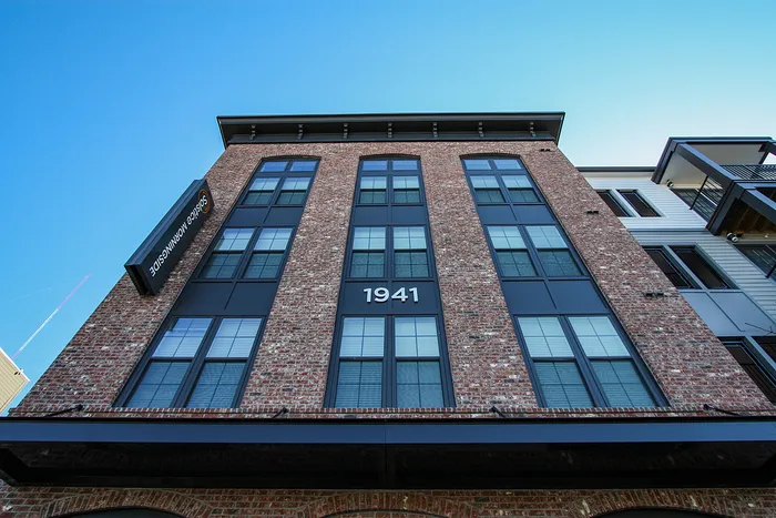Charming brick apartment building with large windows and modern design elements, marked with the number 1941, set against a clear blue sky.