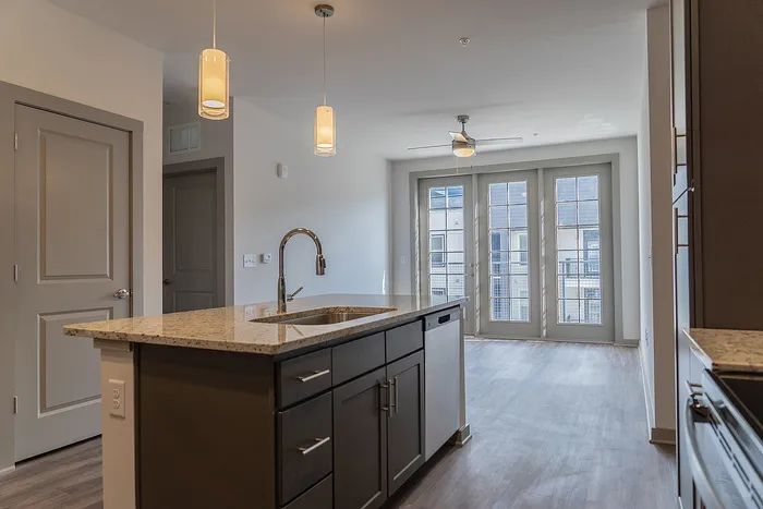 Modern apartment kitchen with sleek granite countertops, stylish island, and bright French doors leading to a sunlit balcony.