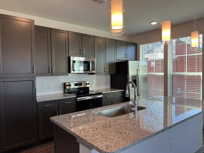 Modern kitchen with sleek dark cabinets, stainless steel appliances, and elegant pendant lighting over a granite island.