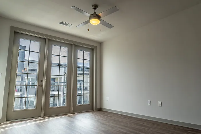 Bright and airy apartment interior featuring large French doors, a modern ceiling fan, and sleek wooden flooring, perfect for stylish urban living.