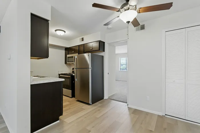 Modern apartment kitchen with sleek stainless steel appliances, dark cabinetry, and bright hardwood floors leading to a cozy living space.