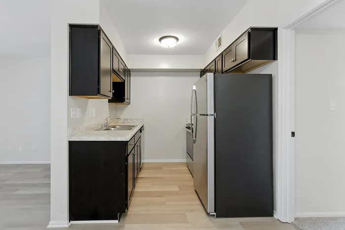 Modern kitchen with sleek black cabinetry, stainless steel refrigerator, and elegant countertops in a bright, open apartment layout.